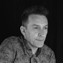 Photo of Jason Conway looking to the right in front of a black background and wearing a floral shirt